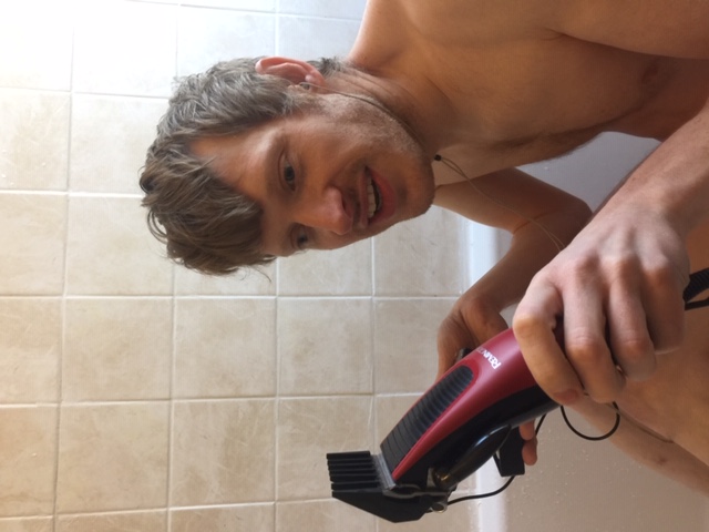 Photo of David sitting in a bath holding a microphone and some hair clippers