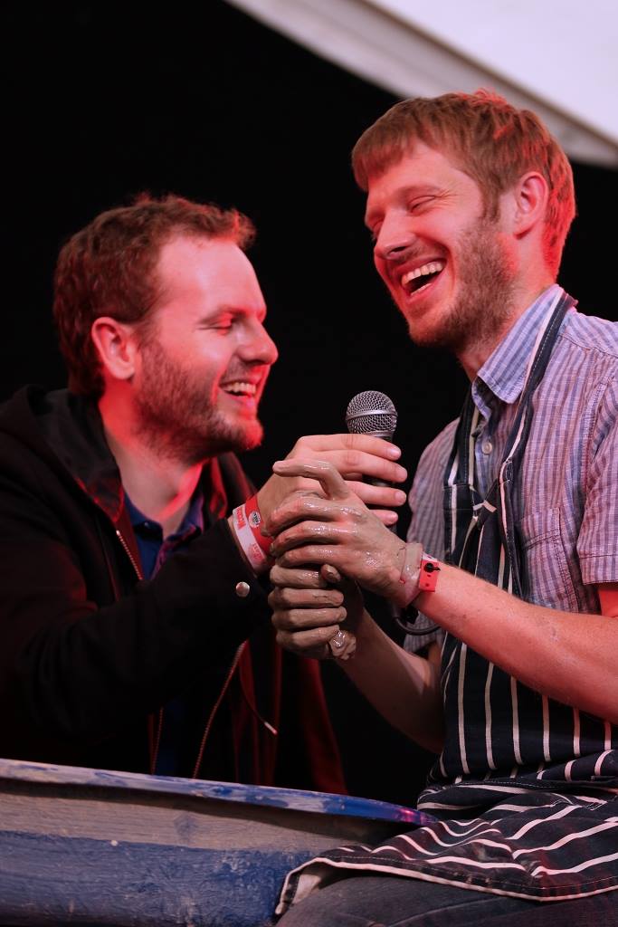 Photo of Sean and David laughing, Sean holding microphone while David does pottery